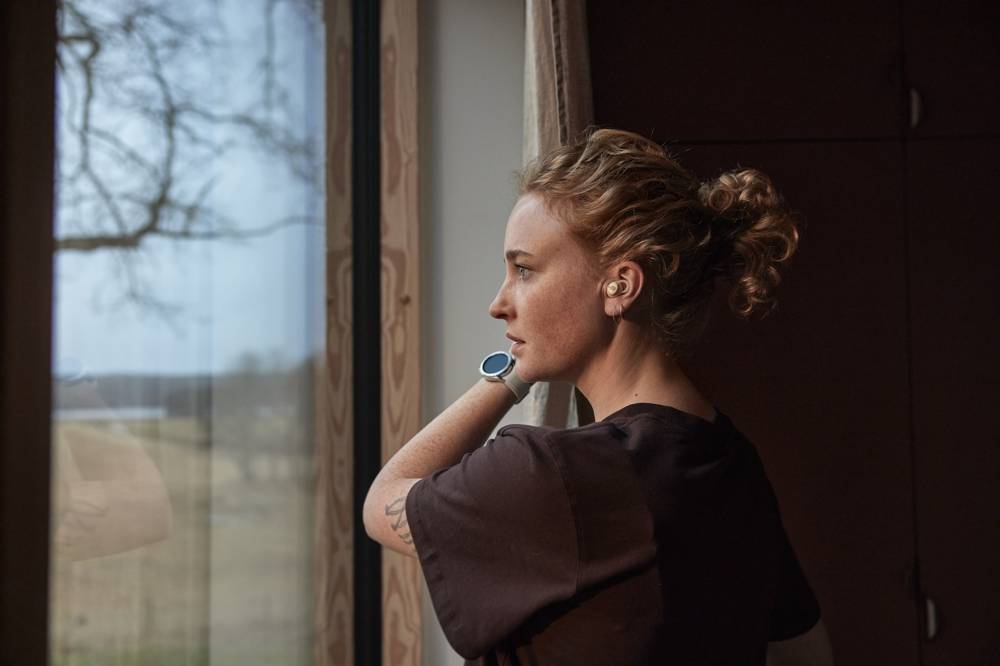 Kvinna står och kollar ut genom fönstret med en smartklocka på armen
