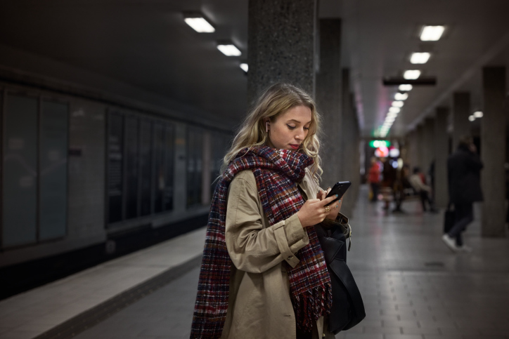 Kvinna på tunnelbaneperrong som tittar på sin mobiltelefon