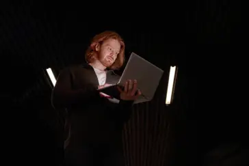 Man som håller och tittar i en laptop i ett mörkt rum.