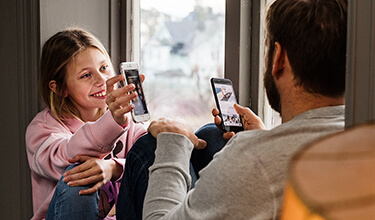 Pappa och barn sitter i fönster med sina mobiler.