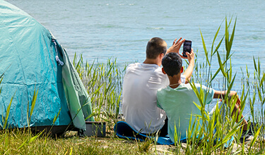 Två pojkar med mobiltelefon utanför tält.