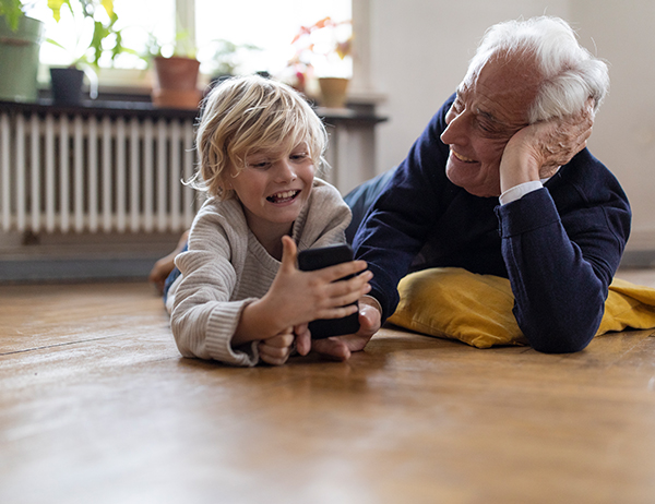 En äldre man och ett barn kollar på mobil och ler