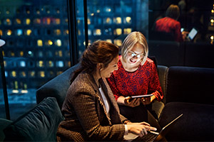 Kvinnor på mörkt kontor med surfplatta och laptop