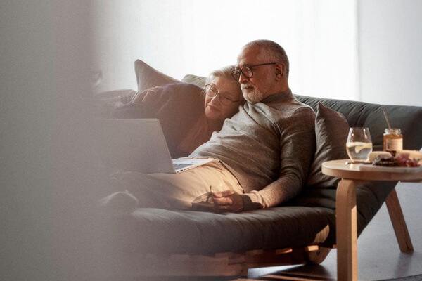 Man och kvinna ligger i soffan och tittar på film på en laptop-dator.