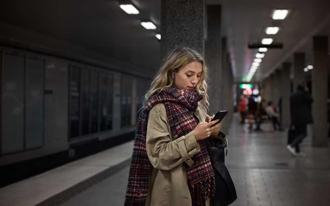 Kvinna på tunnelbaneperrong som tittar på sin mobiltelefon