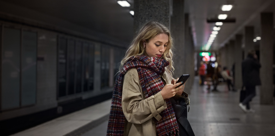 Kvinna på tunnelbaneperrong som tittar på sin mobiltelefon