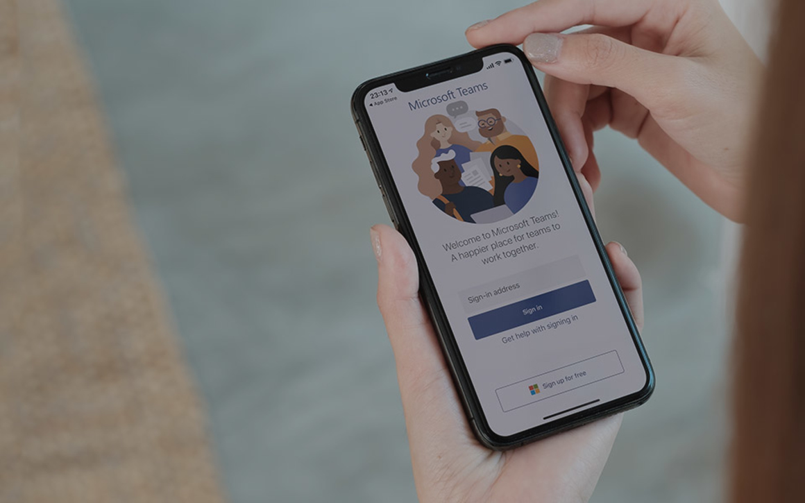 Hand håller i mobil med Microsoft Teams på skärmen.