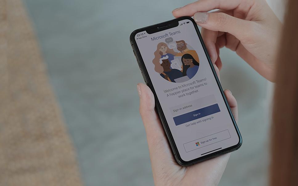 Hand håller i mobil med Microsoft Teams på skärmen.