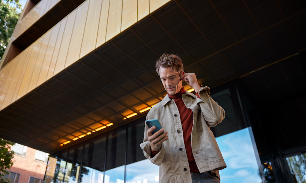 Man med hörlurar och mobil framför en byggnad