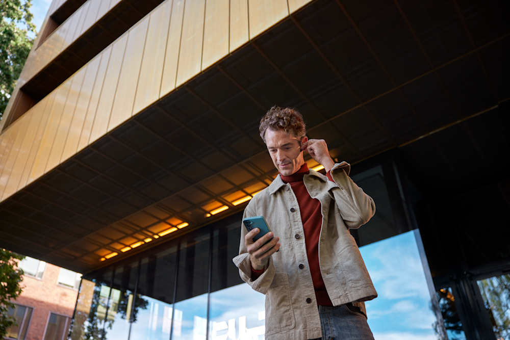 Man med hörlurar och mobil framför en byggnad