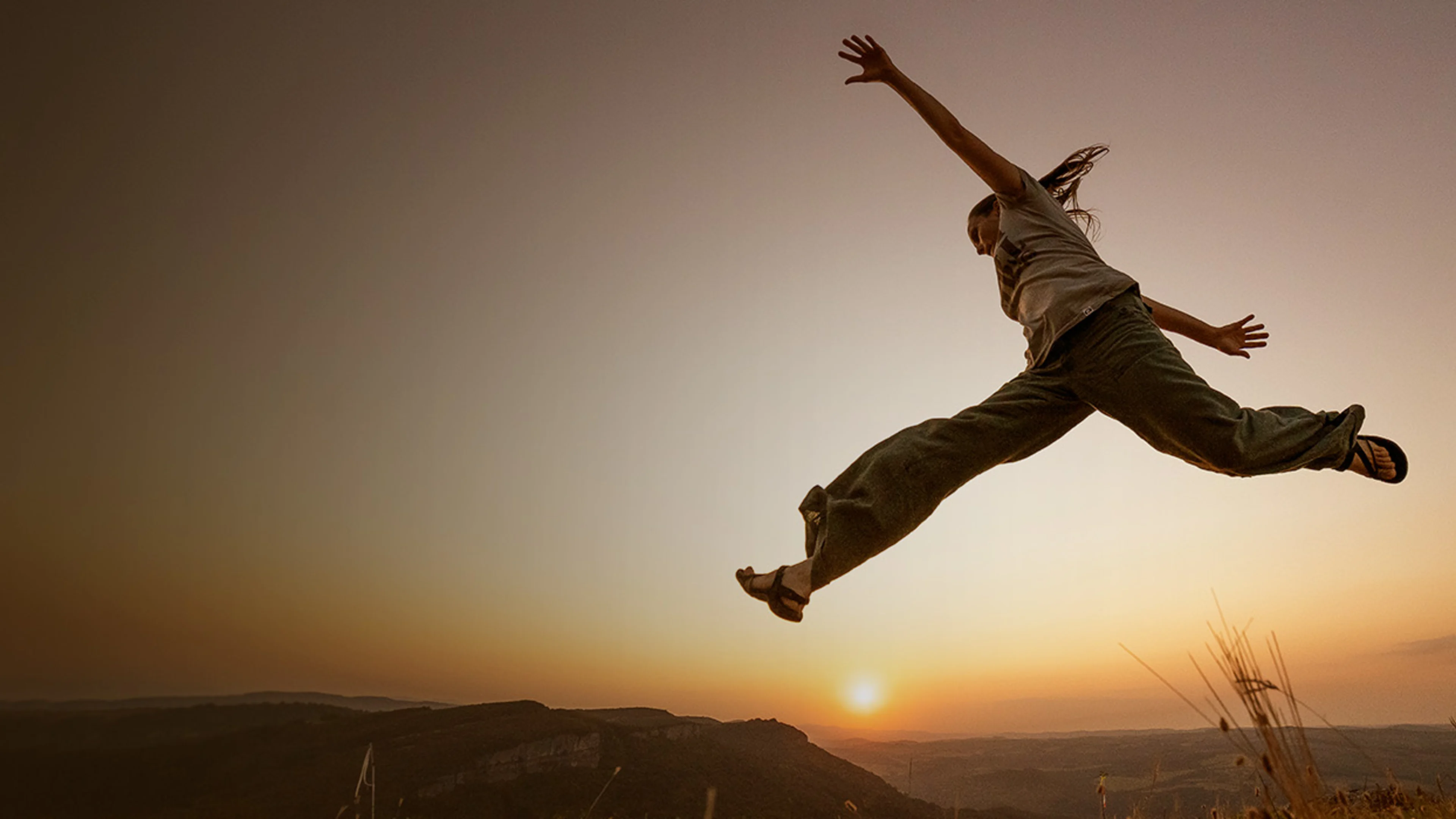 Kvinna som hoppar bland berg med solnedgång i bakgrunden
