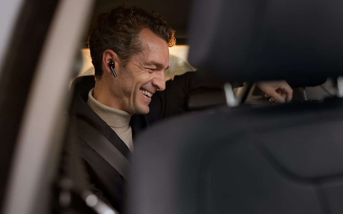 Leende man med hörlur i örat i baksätet använder VPN.