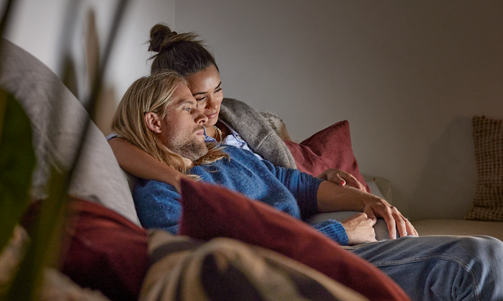 Ett yngre par sitter tillsammans i soffan och tittar på tv.