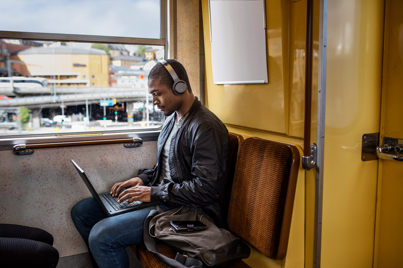 Kille på tunnelbanan med laptop och hörlurar