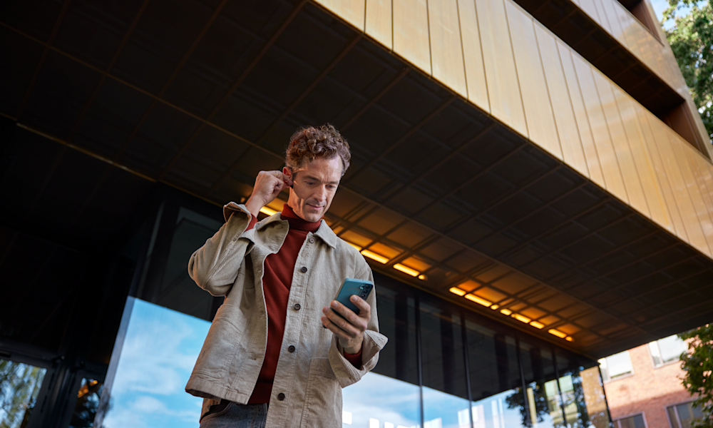 Manlig företagare pratar i mobil med hörlurar utomhus.