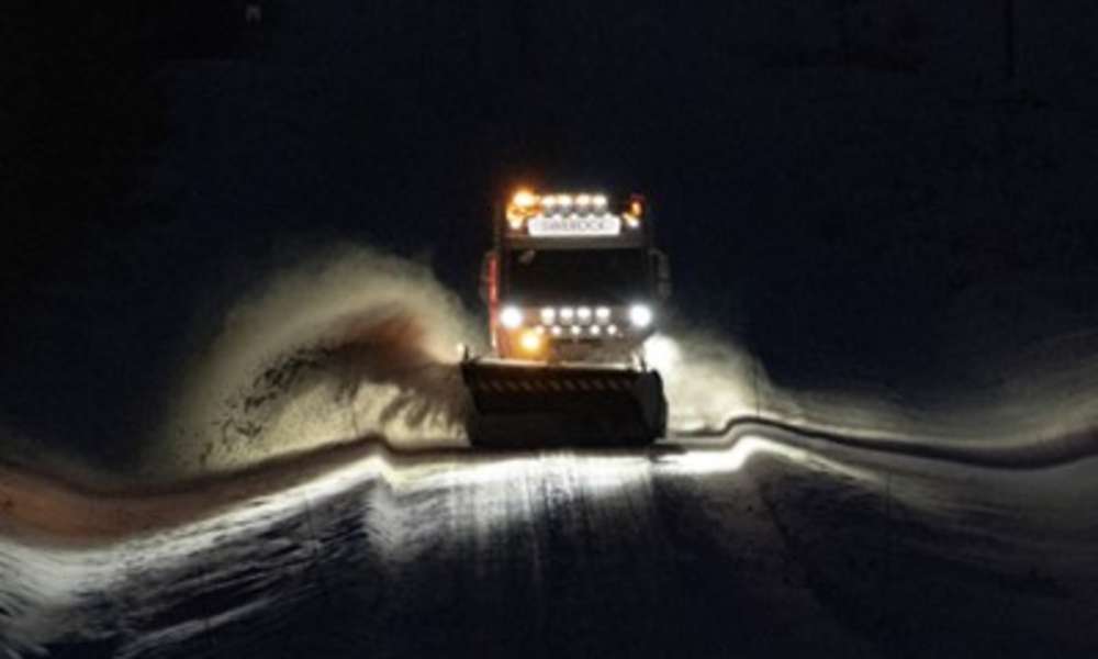 Lastbil som plogar snö från en väg i mörker