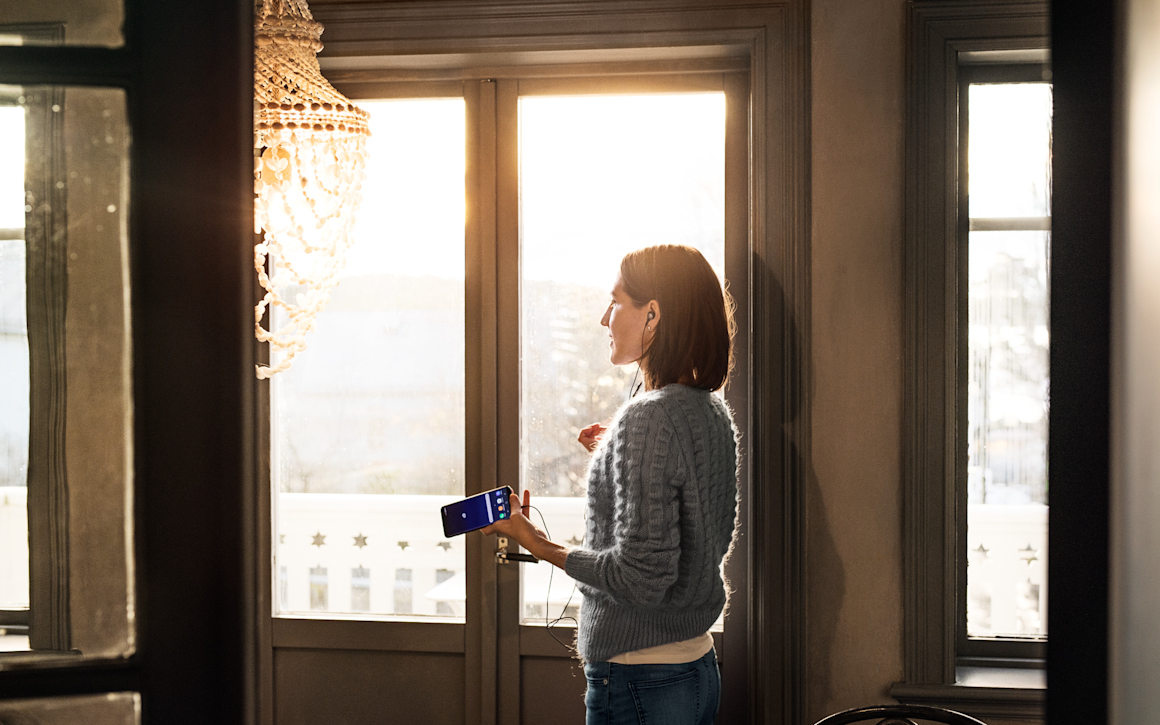 Kvinna håller telefon i handen och pratar med hörlurar.