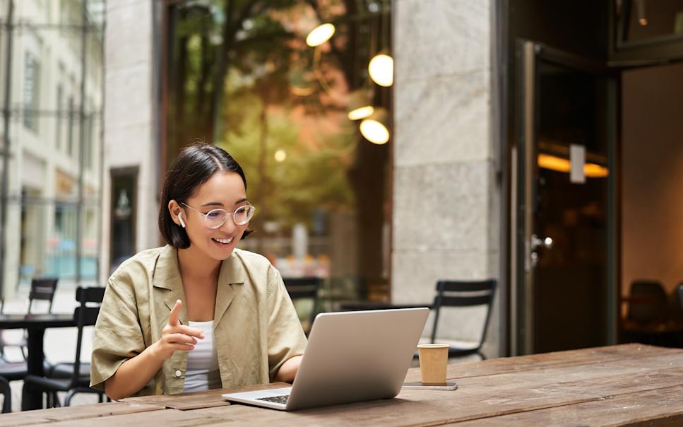 Ung kvinna arbetar med laptop med mobilt bredband utomhus på café.