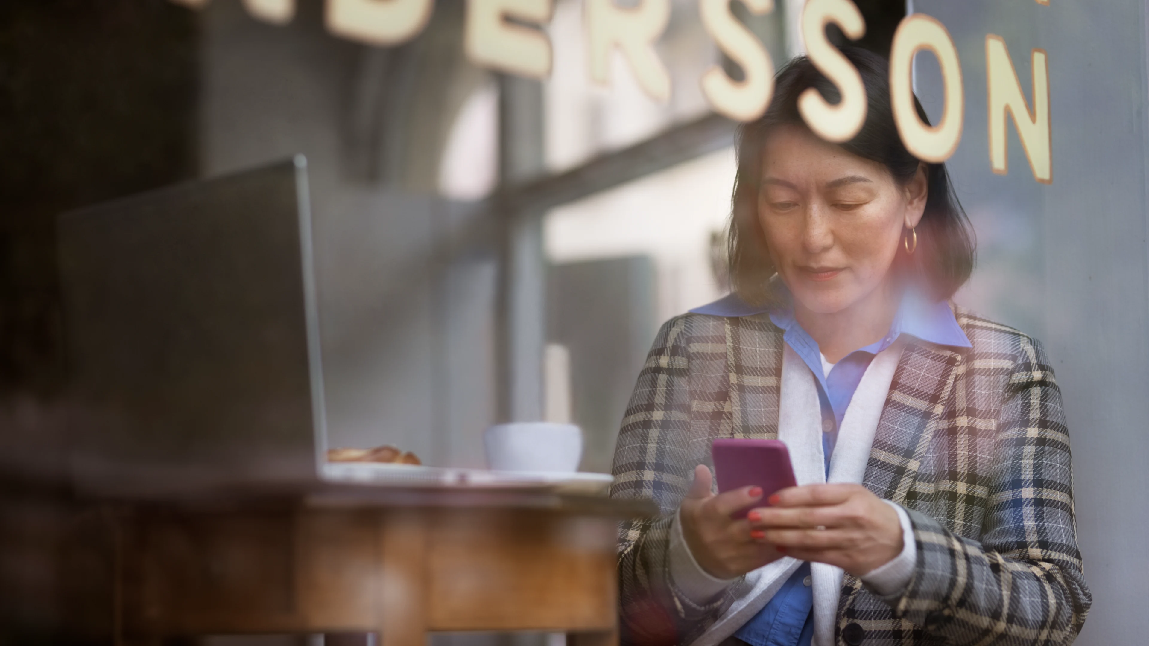 Mörkhårig kvinna med arbetar på cafe med mobil och laptop.