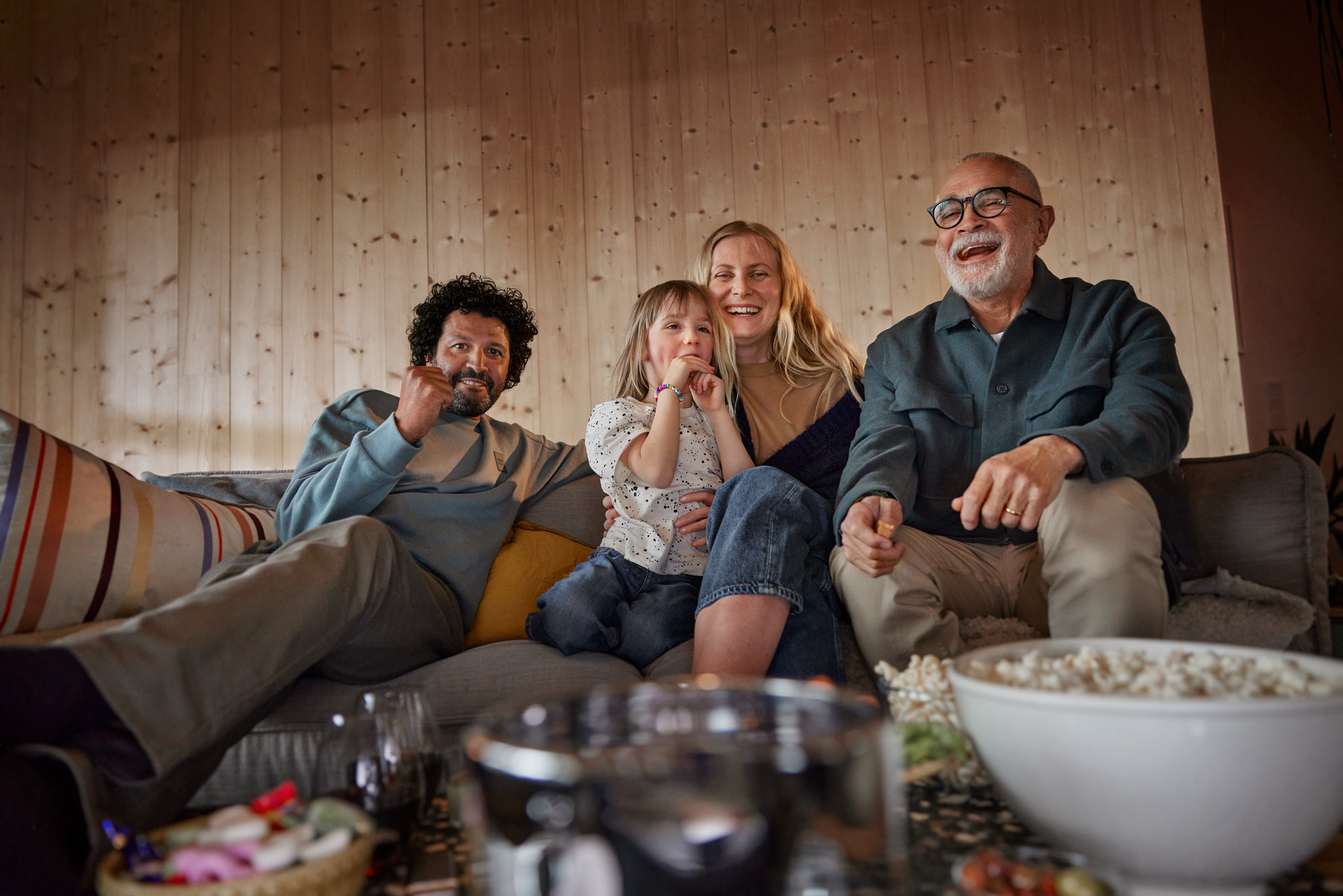 En glad familj tittar på tv och äter popcorn. 