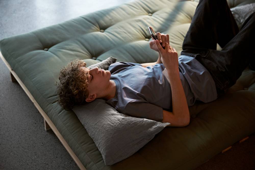 Ung kille ligger och tittar på mobilen.