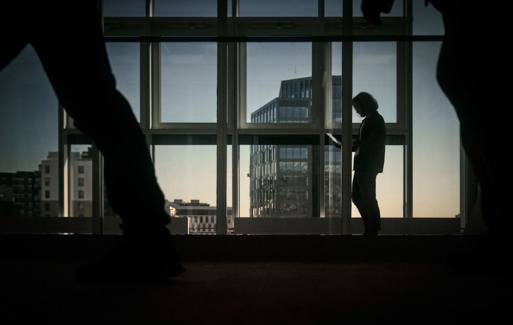 Silhuett av man som går framför kontorsfönster i ett mörkt rum