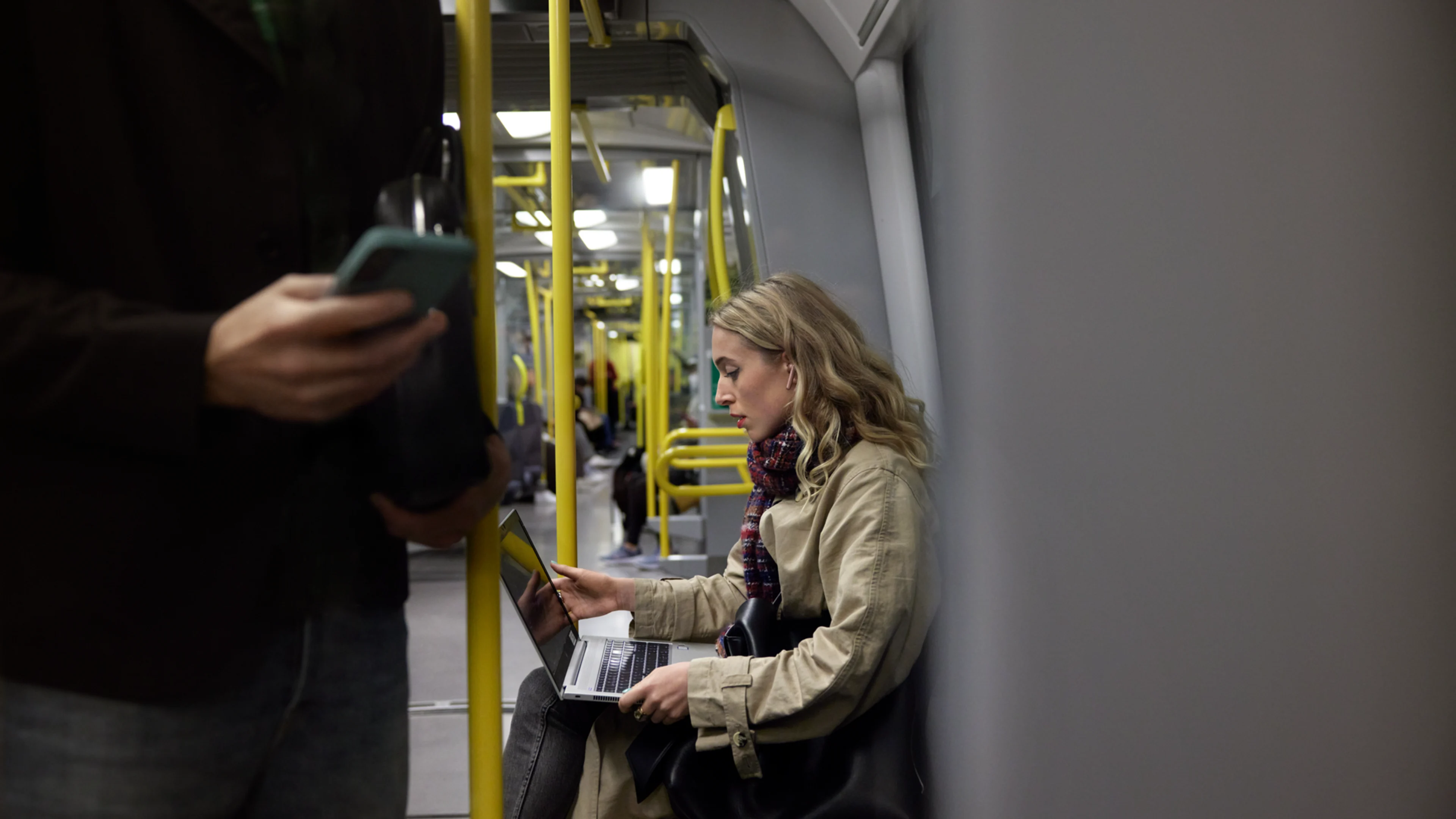 Blond kvinna åker tunnelbana med laptop i knät.