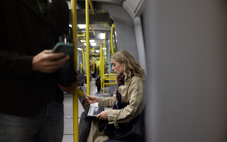 Blond kvinna åker tunnelbana med laptop i knät.