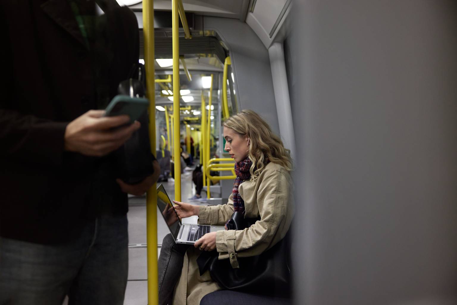 Blond kvinna åker tunnelbana med laptop i knät.