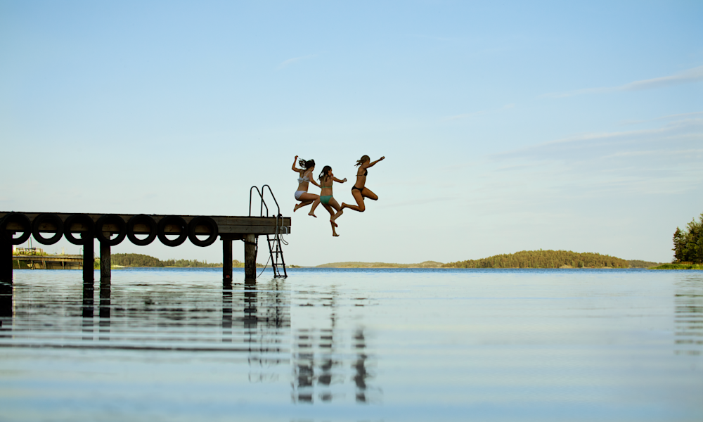 Tre flickor badar från brygga