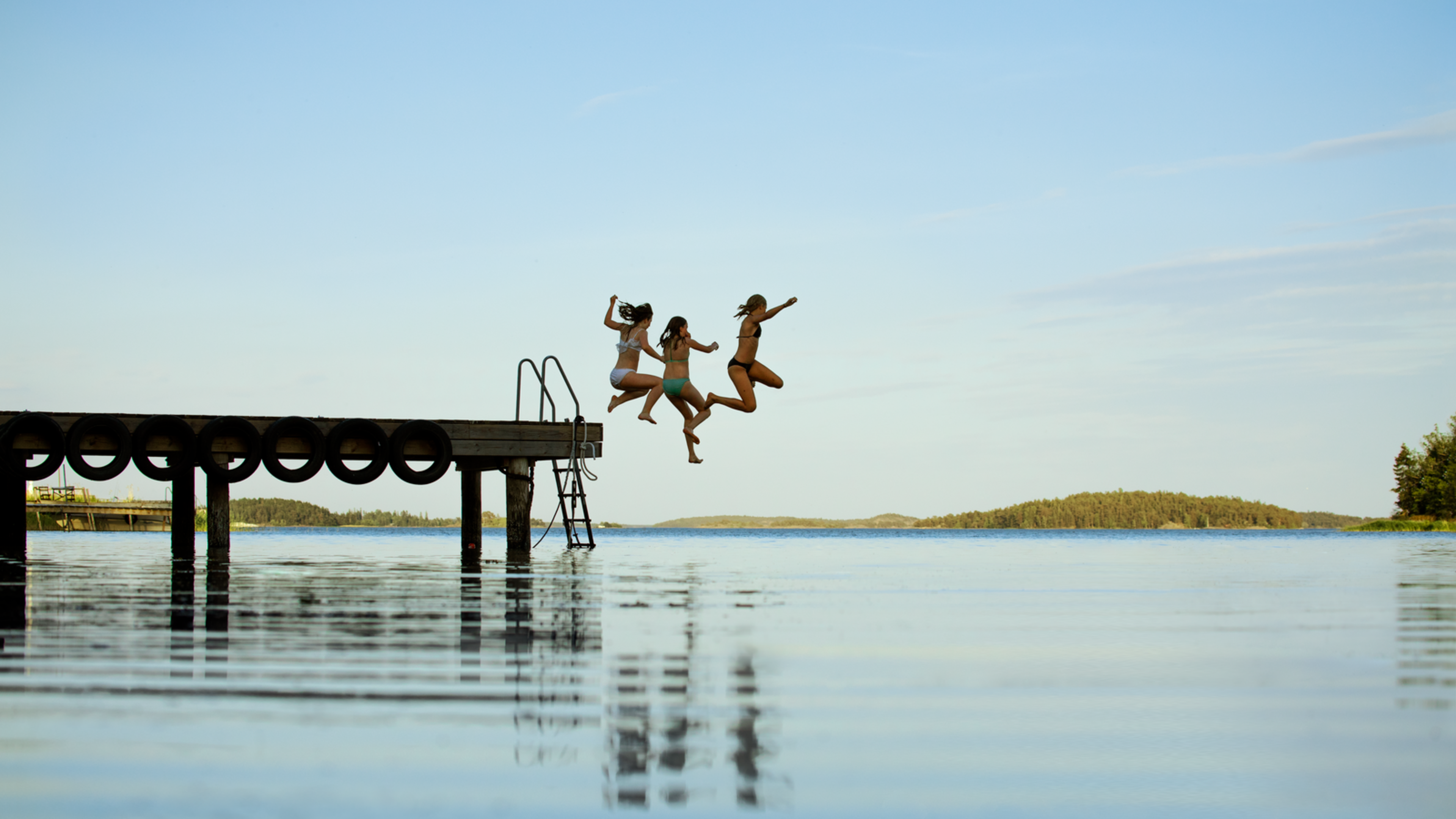 Tre flickor badar från brygga