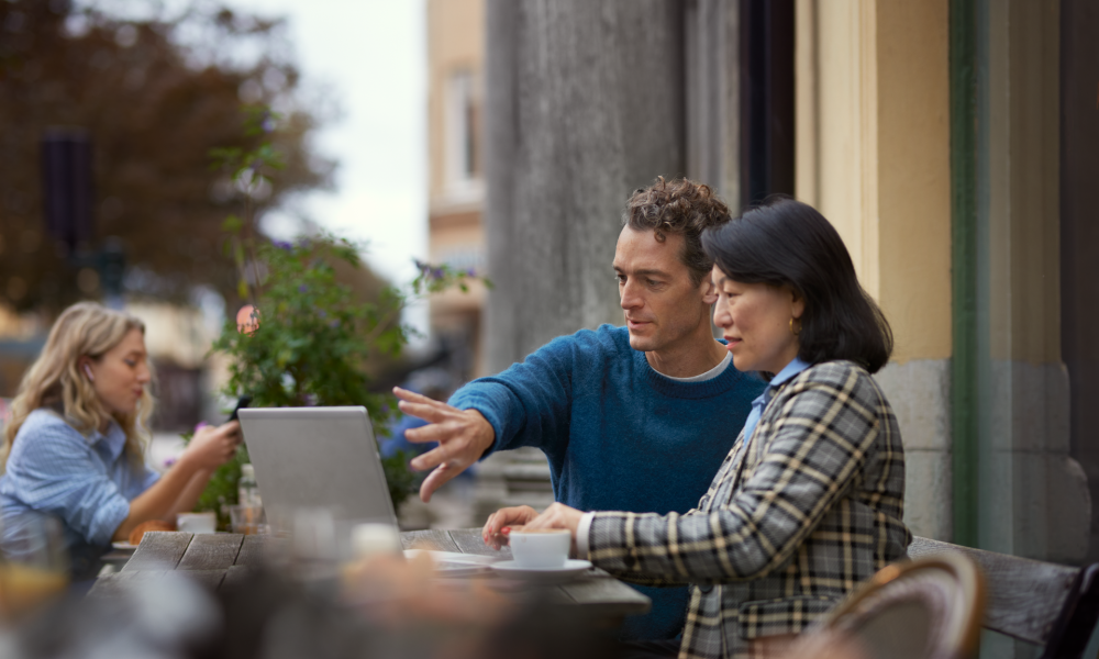 Man visar kvinna på en laptop på café utomhus.