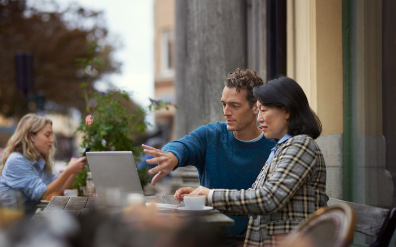 Man och kvinna arbetar på laptop på café utomhus.