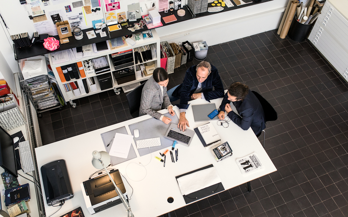 Tre personer runt ett bord i kontorsmiljö, fågelperspektiv.