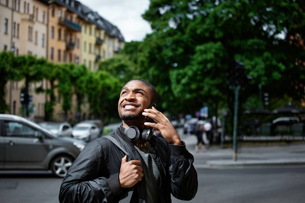 Man som ler och pratar i mobil och kollar upp mot himlen
