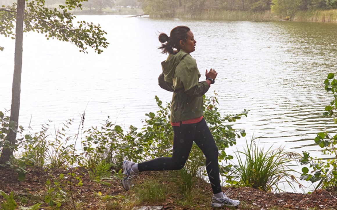 Kvinna joggar i skogen framför sjö.