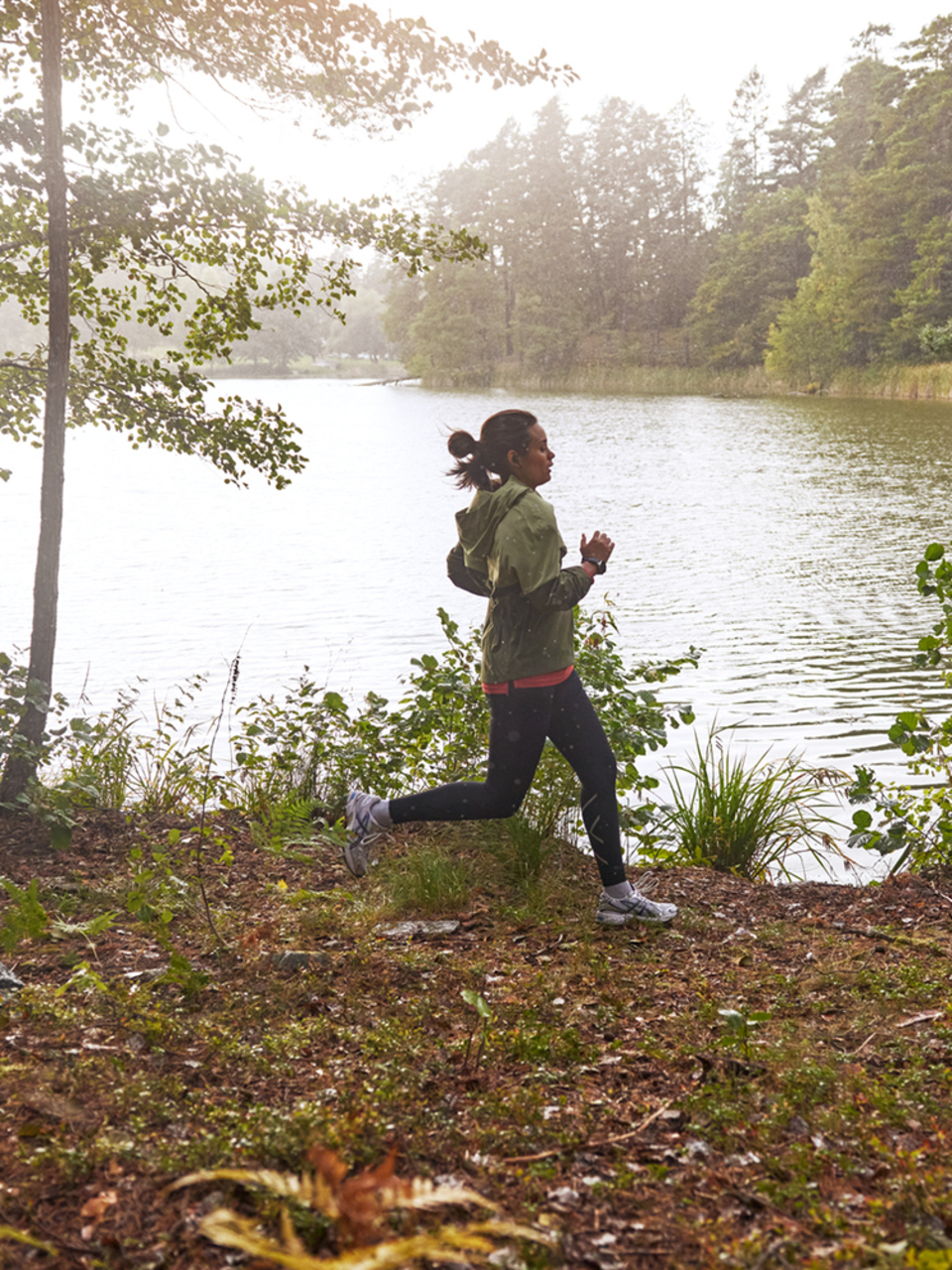 Kvinna joggar i skogen framför sjö.