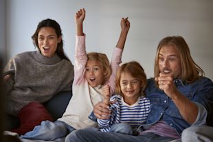 En glad familj tittar på tv och äter popcorn.