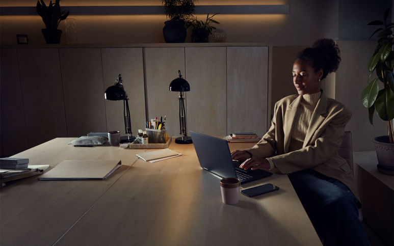 Kvinna i kavaj med take away-kaffe arbetar med laptop på kontor