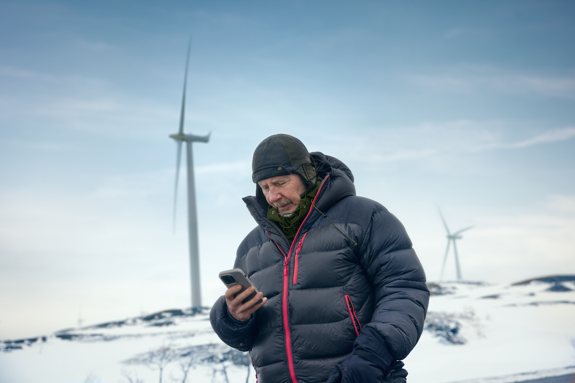 Man med dunjacka, mössa och mobil i vinterlandskap