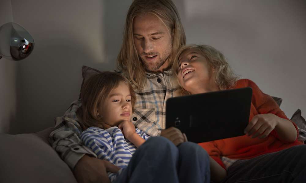 Man och två barn tittar på en platta i soffa
