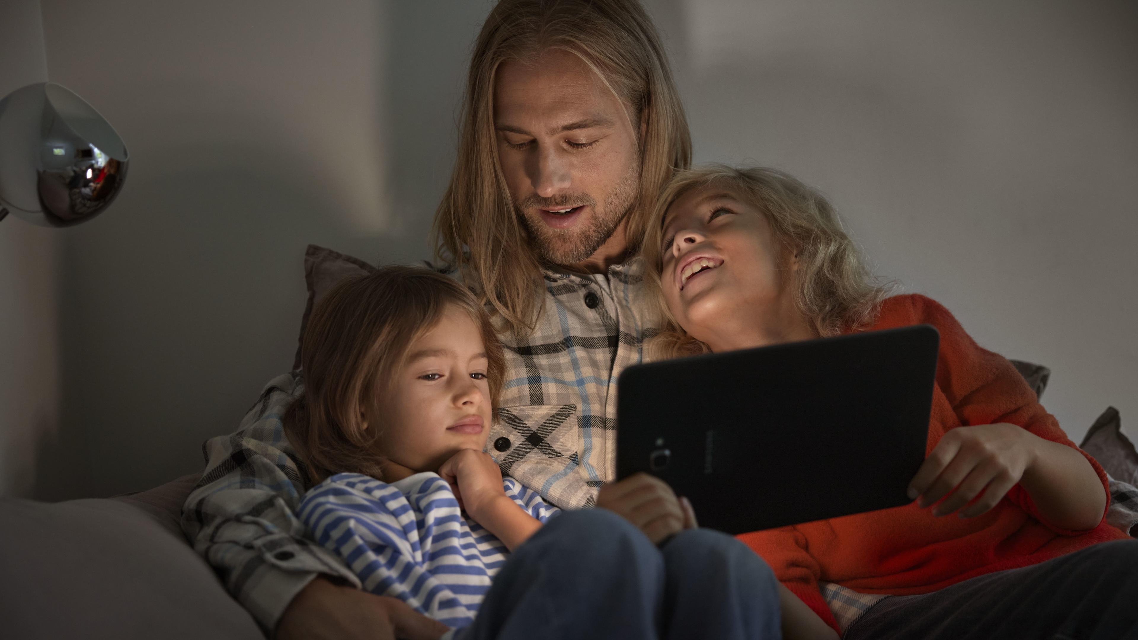 Man och två barn tittar på en platta i soffa