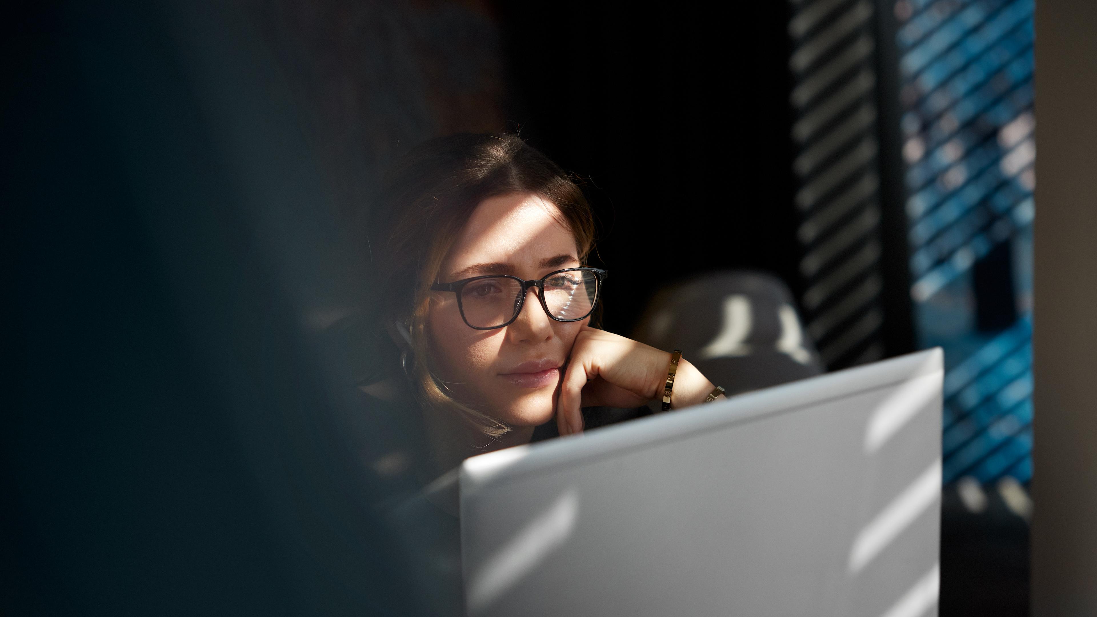 Kvinna som betraktar dataskärm med handen mot hakan.