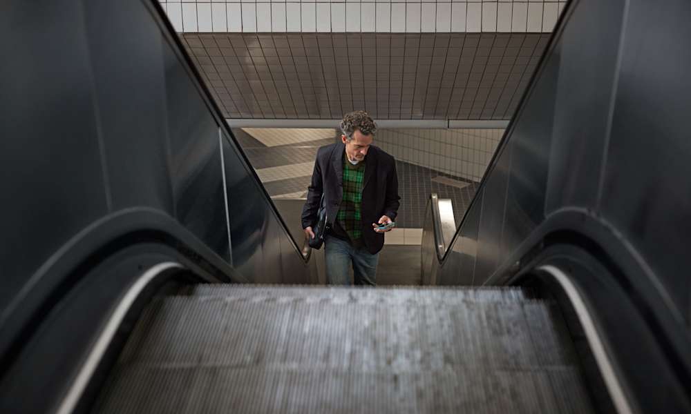 Man som åker rulltrappa och tittar på sin telefon.