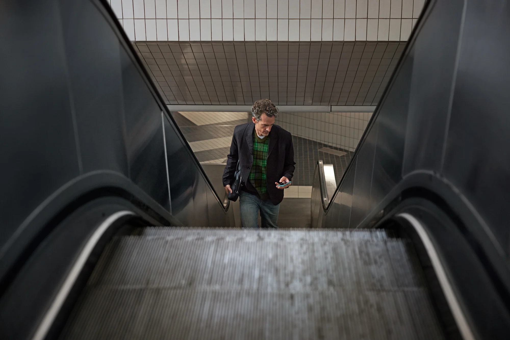 Man som åker rulltrappa och tittar på sin telefon.