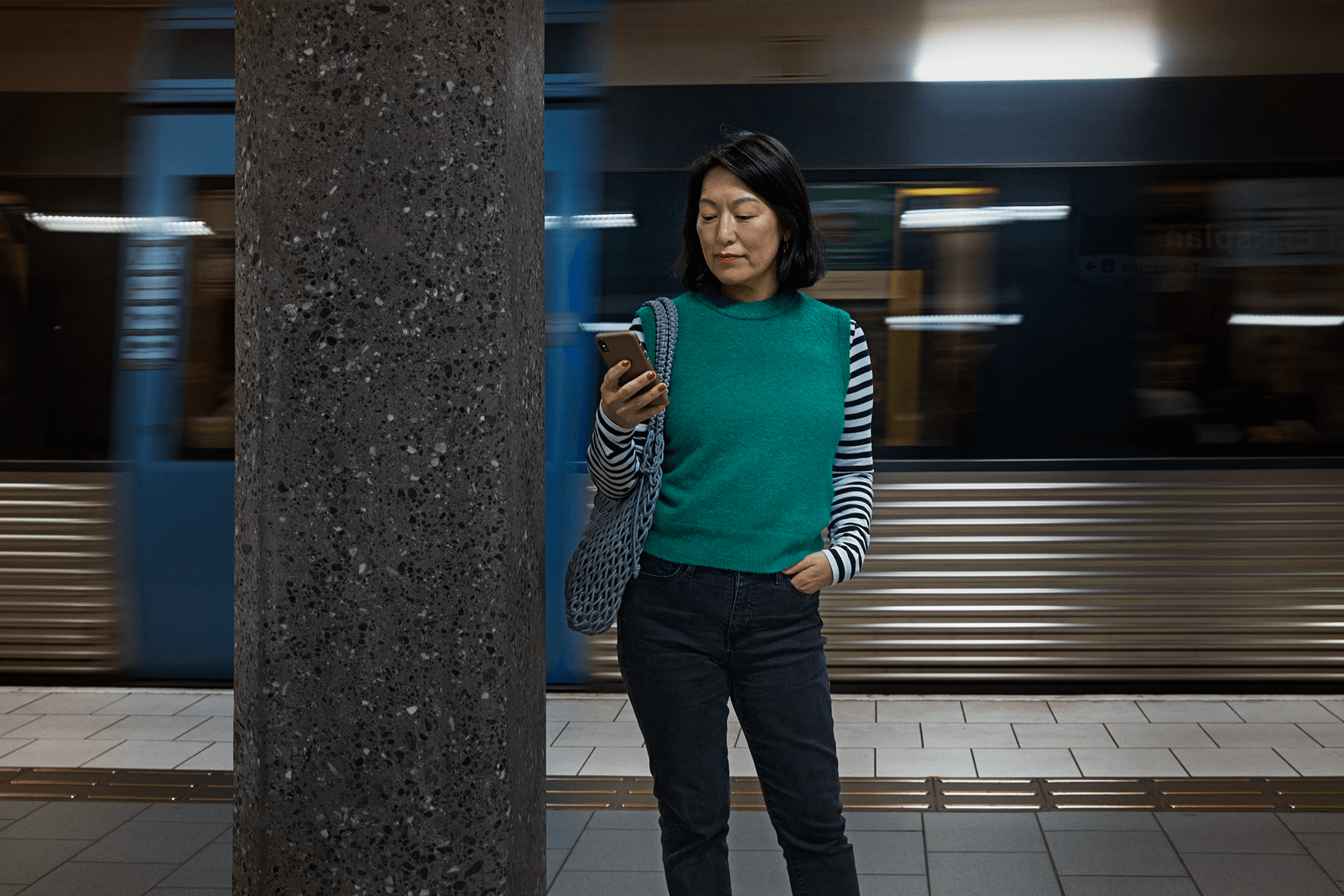 Kvinna kollar på sin mobil på tunnelbaneperrongen