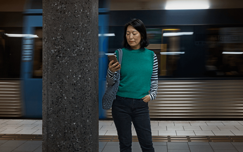 Kvinna som står och kollar på sin mobil på en tunnelbaneperrong.