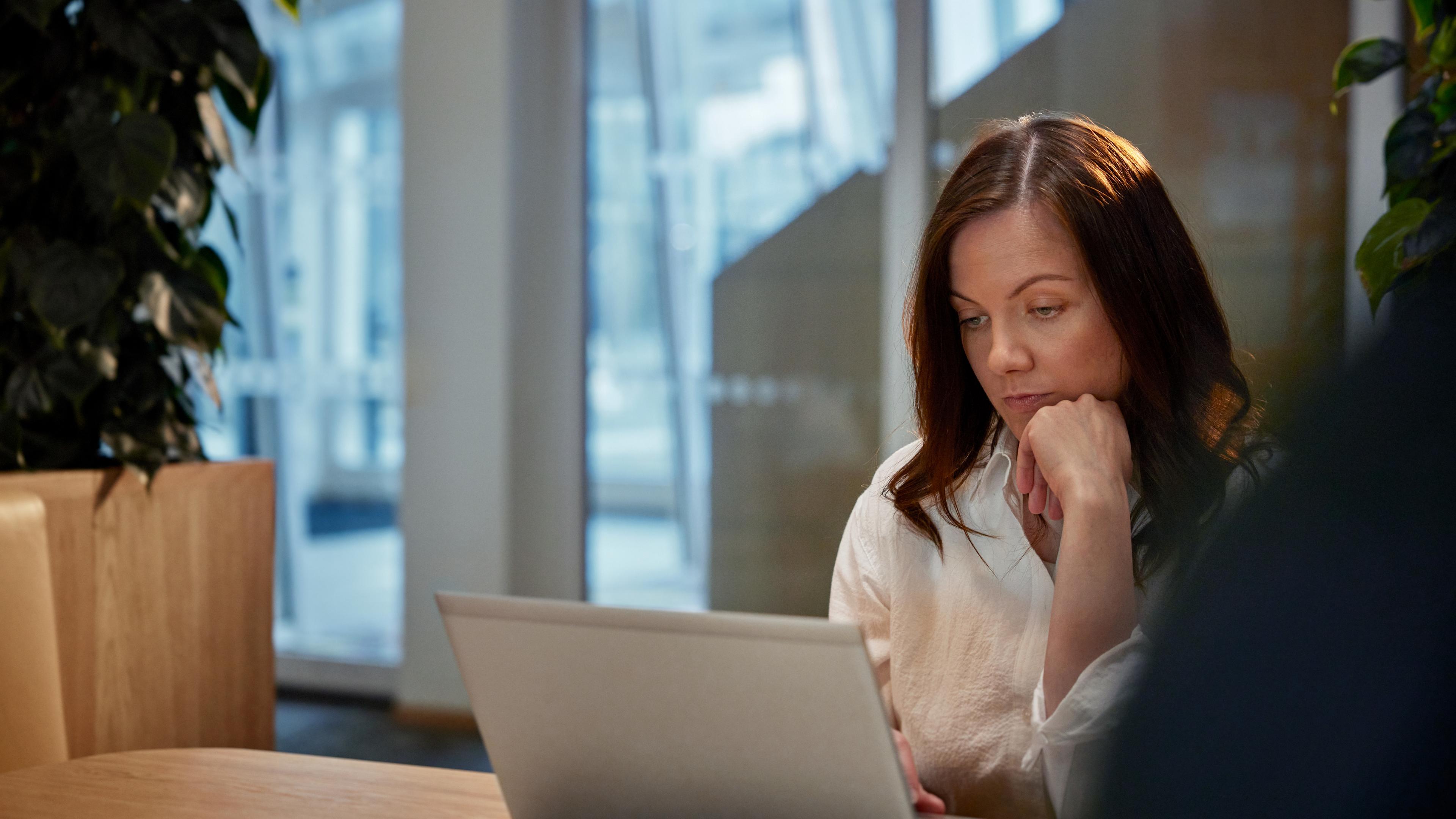 Kvinna som betraktar datorskärm med handen på hakan.