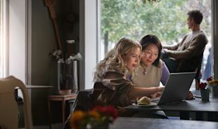 Två personer på café sitter framför laptop tillsammans. 