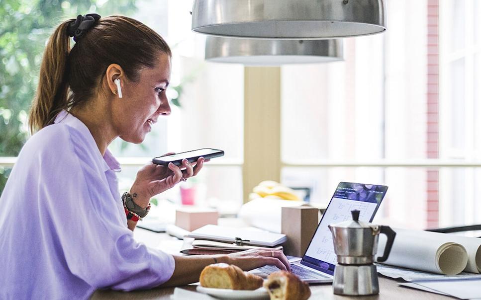 Kvinna med mobiltelefon arbetar vid laptop.